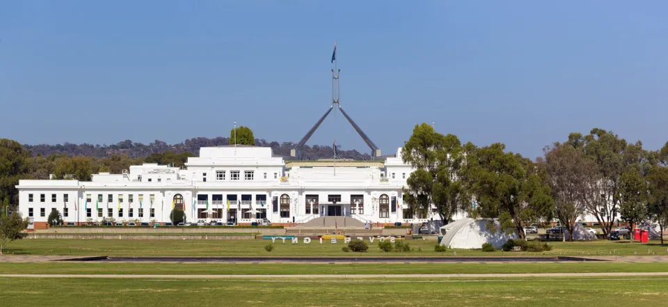 Old Parliament House, with flagpole of new parliament building in the background and Aboriginal Tent Embassy in front of it